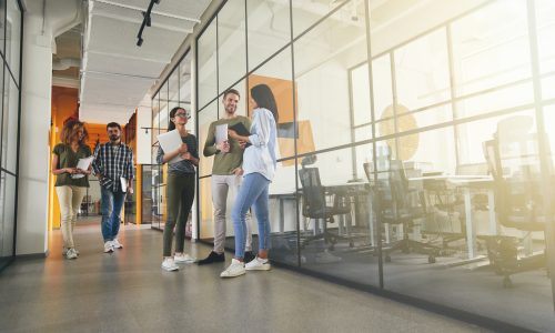 Copy space photo of five young people with laptops chatting and hanging out in a workplace hallway